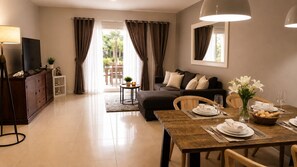A modern living room with a sofa, a dining table set for two, and a television on a cabinet.