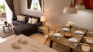 A modern living room with a sofa, dining table set for two, and a small side table with a lamp.