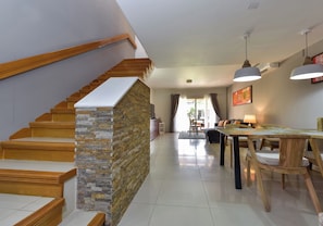 Ein modernes Interieur mit einer Holztreppe, einem Essbereich mit Holztisch und -stühlen sowie Blick ins Freie durch eine Glastür.