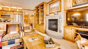 A cozy living room with a fireplace, wooden cabinets, a television, and a dining area. - Heart Of River Run & Spacious 2br Premier 2 Bedroom Condo by RedAwning (Keystone)