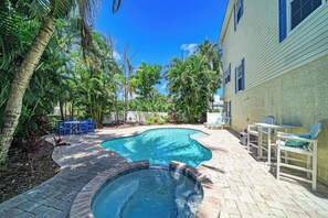 Ein Garten mit Swimmingpool, umgeben von Palmen und einer Terrasse mit Gartenmöbeln.