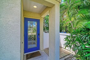 Uma porta azul com painel de vidro, parede branca com textura e um pequeno alpendre com grade branca.