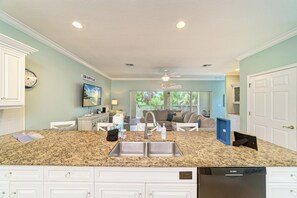 A kitchen with granite countertops, a dishwasher, and a dining area with a sofa and a TV.