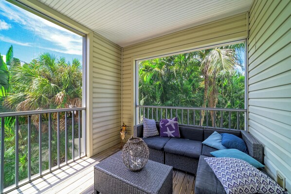 A balcony with a wicker sofa, cushions, and a woven basket.