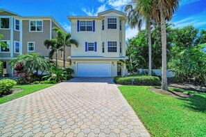 A two-story residential building with a garage, surrounded by well-maintained landscaping and a paved driveway.