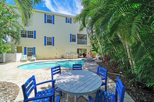 A two-story house with a swimming pool, outdoor seating, and tropical vegetation.