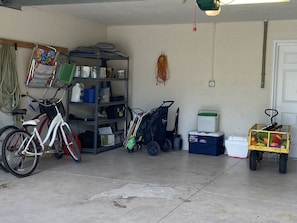 Eine Garage mit Fahrrad, Wagen, Wasserspender und Regallagerung mit diversen Gegenständen.