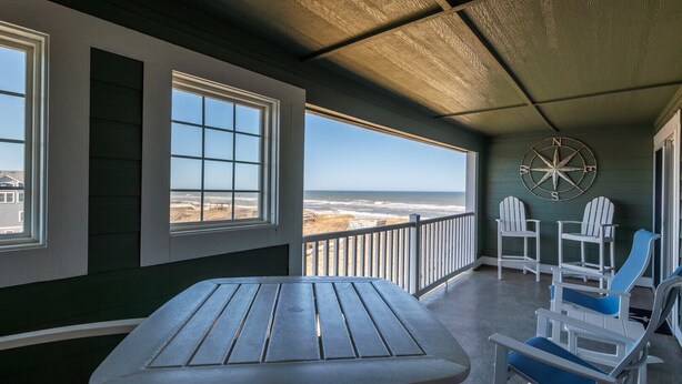 A balcony with a table and chairs, a compass wall decoration, and a view of the beach.