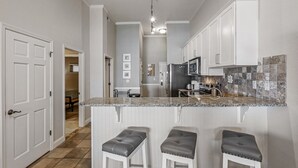 A modern kitchen with white cabinetry, a granite countertop, and a stainless steel refrigerator.