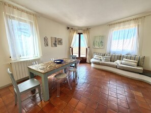 A room with a dining table, chairs, a sofa, and a window with curtains.