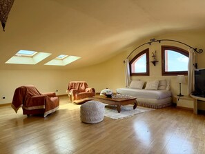 A spacious loft bedroom with a high ceiling, skylights, a sofa, a TV, and a coffee table.
