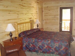 Ein Schlafzimmer in einer Holzhütte mit einem Bett, zwei Nachttischlampen, einem Holzkopfstück und einer Tür zu einem Außenbereich.