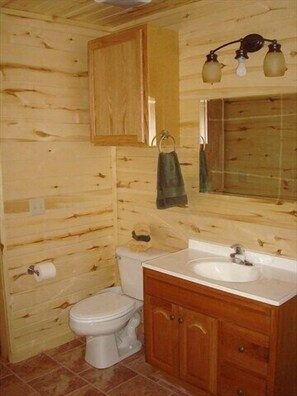 Ein Badezimmer mit Holzwandverkleidung, Toilette, Waschbecken und Schrank.