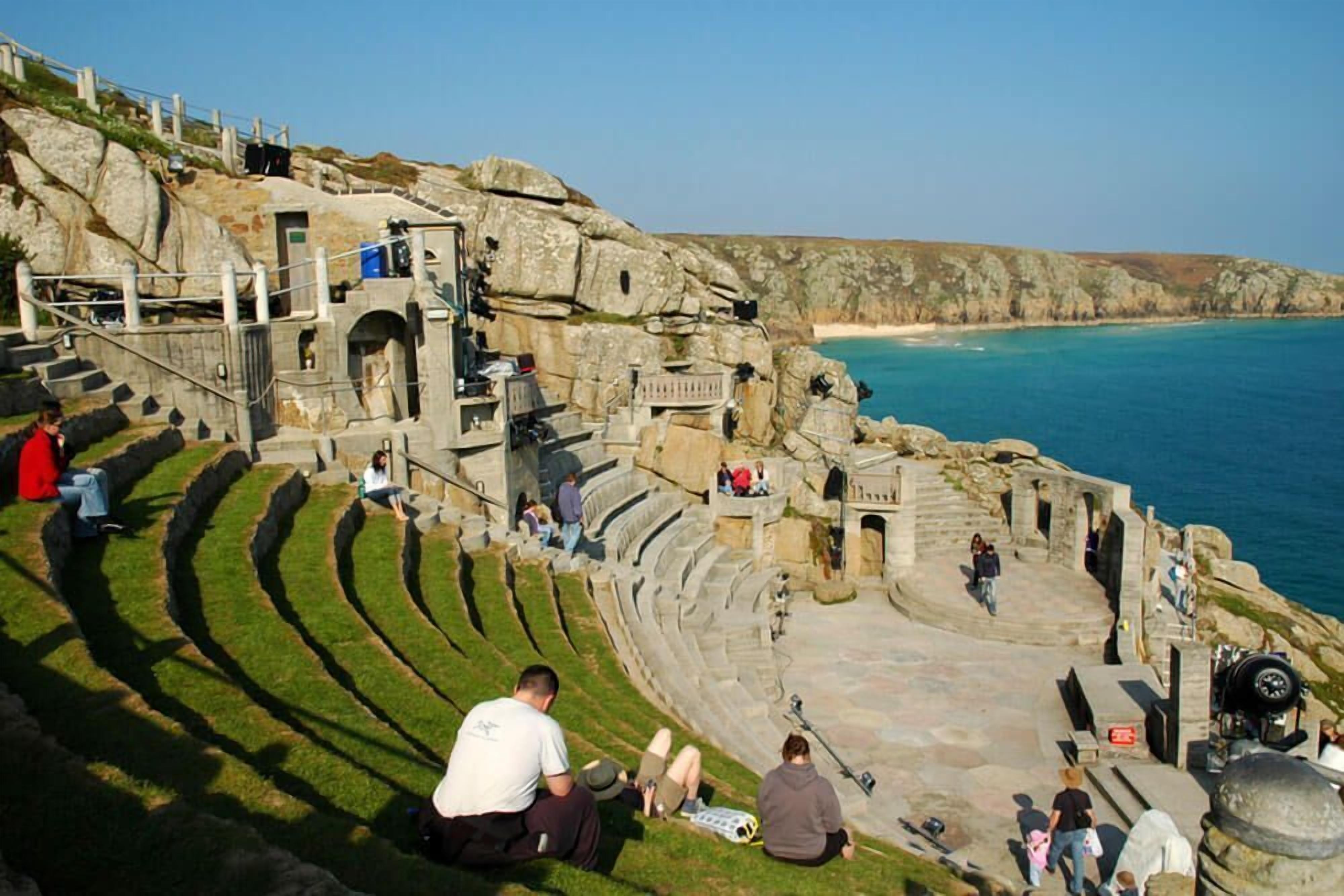 Ein historisches Amphitheater mit gestuften Sitzreihen, Steinarchitektur und Blick auf das Meer.