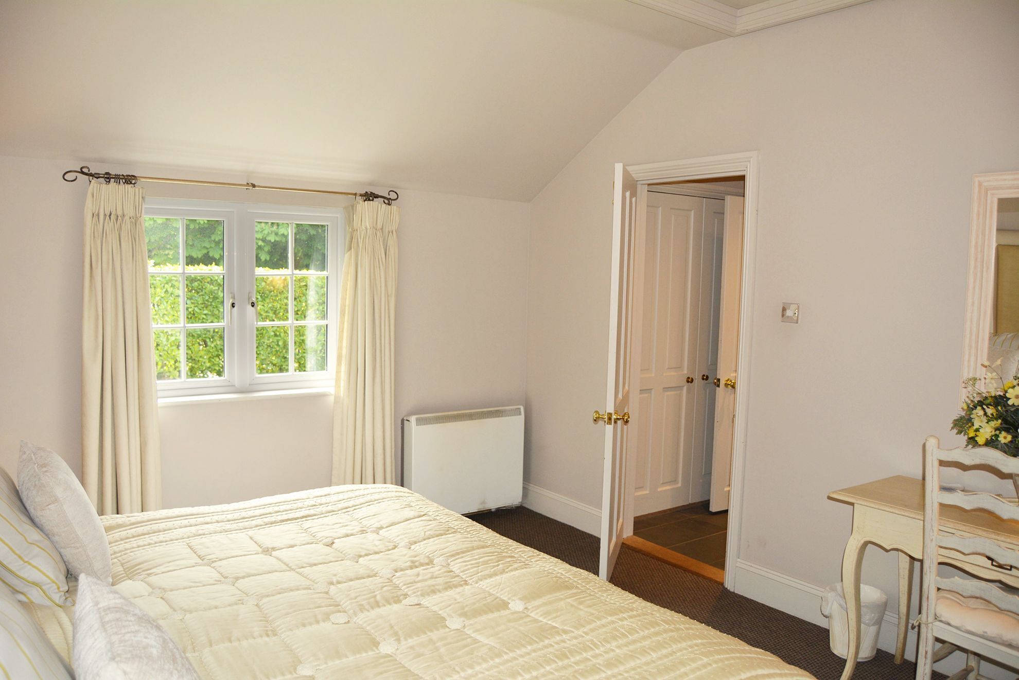 Een slaapkamer met een bed, een radiator, een deur naar een andere kamer, en een klein tafeltje met een spiegel.