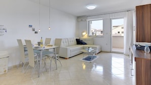 A modern living room with a glass dining table, white sofa, and a view of the outside through large windows.