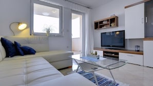 A modern living room with a sofa, a glass coffee table, a TV, and a wooden shelf.