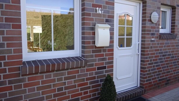 A brick building with a white door, a mailbox, and a small potted plant. - Stylish and native: The tastefully furnished semi-detached house provides a (Carolinensiel)