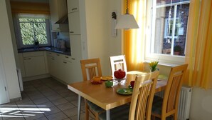 A dining area with a wooden table and chairs, a window with yellow curtains, and a view of the outside. - Stylish and native: The tastefully furnished semi-detached house provides a (Carolinensiel)