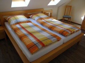 A bedroom with a wooden bed, two pillows, a nightstand, a chair, and a skylight. - Stylish and native: The tastefully furnished semi-detached house provides a (Carolinensiel)