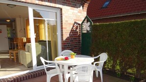 A patio with a round table and four white chairs, a potted plant, and a small table with a bowl and a red cup. - Stylish and native: The tastefully furnished semi-detached house provides a (Carolinensiel)