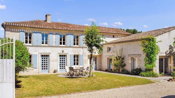A two-story house with a tiled roof, a well-maintained lawn, and a dining area with outdoor furniture.