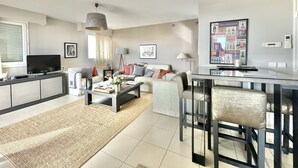 A modern living room with a sofa, coffee table, and TV. There is a dining area with chairs and a table. - Bristol (Cannes)