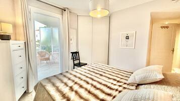 Une chambre à coucher comprenant un lit, une chaise, un bureau et une porte donnant sur un balcon.