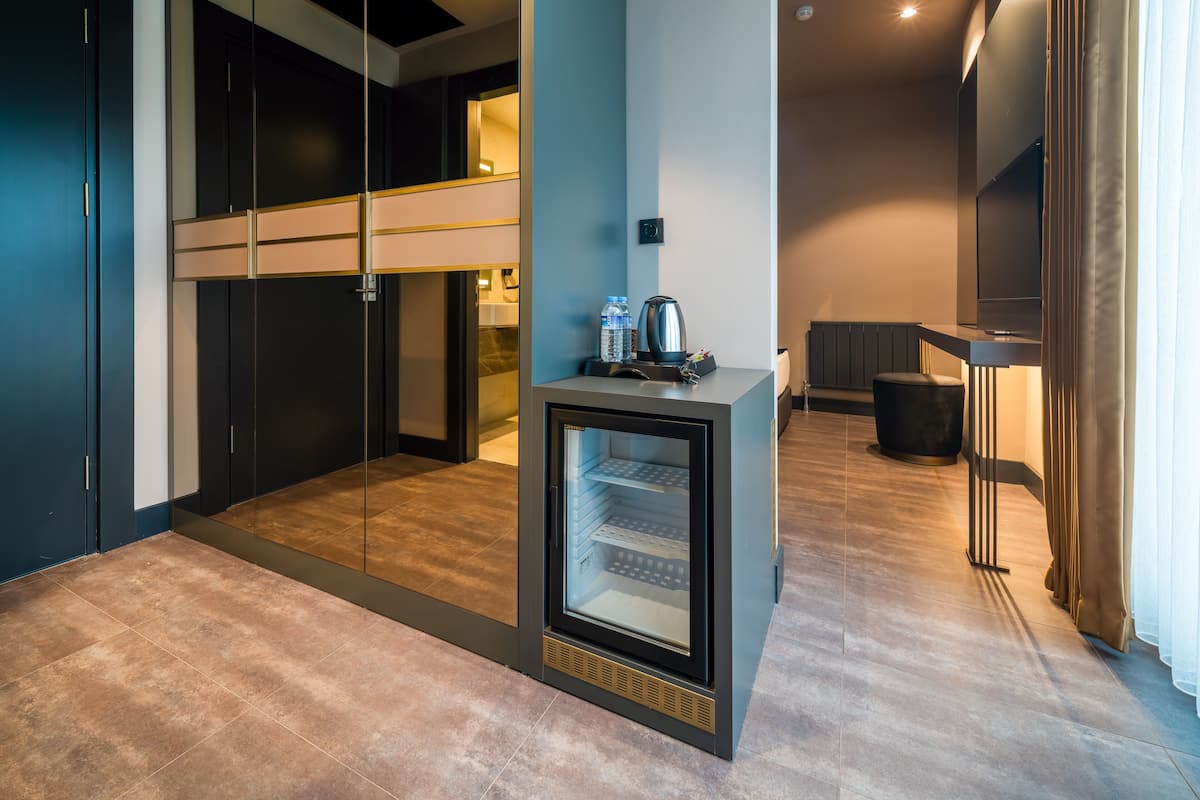 A modern hotel room with a minibar, a glass-enclosed closet, and a seating area with a TV.