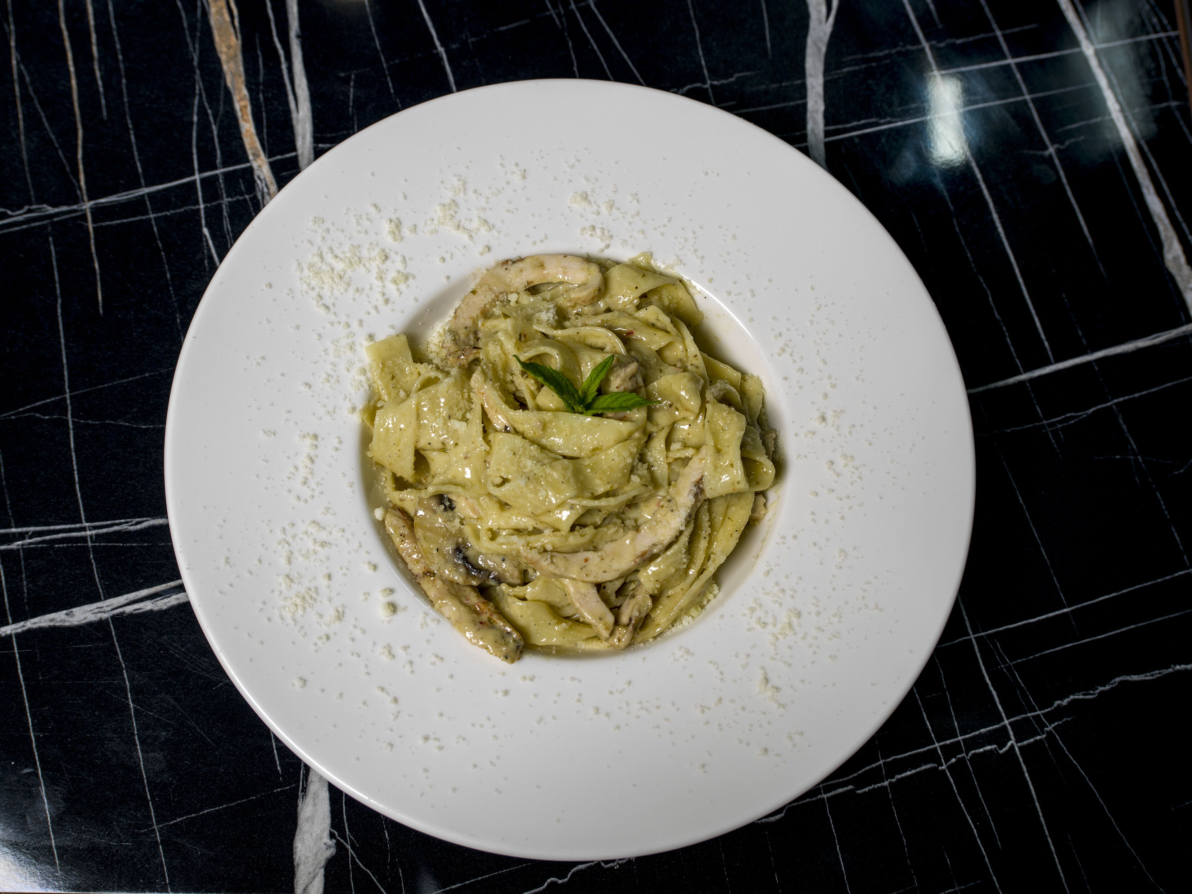 A white plate with a creamy pasta dish on a black marble surface.