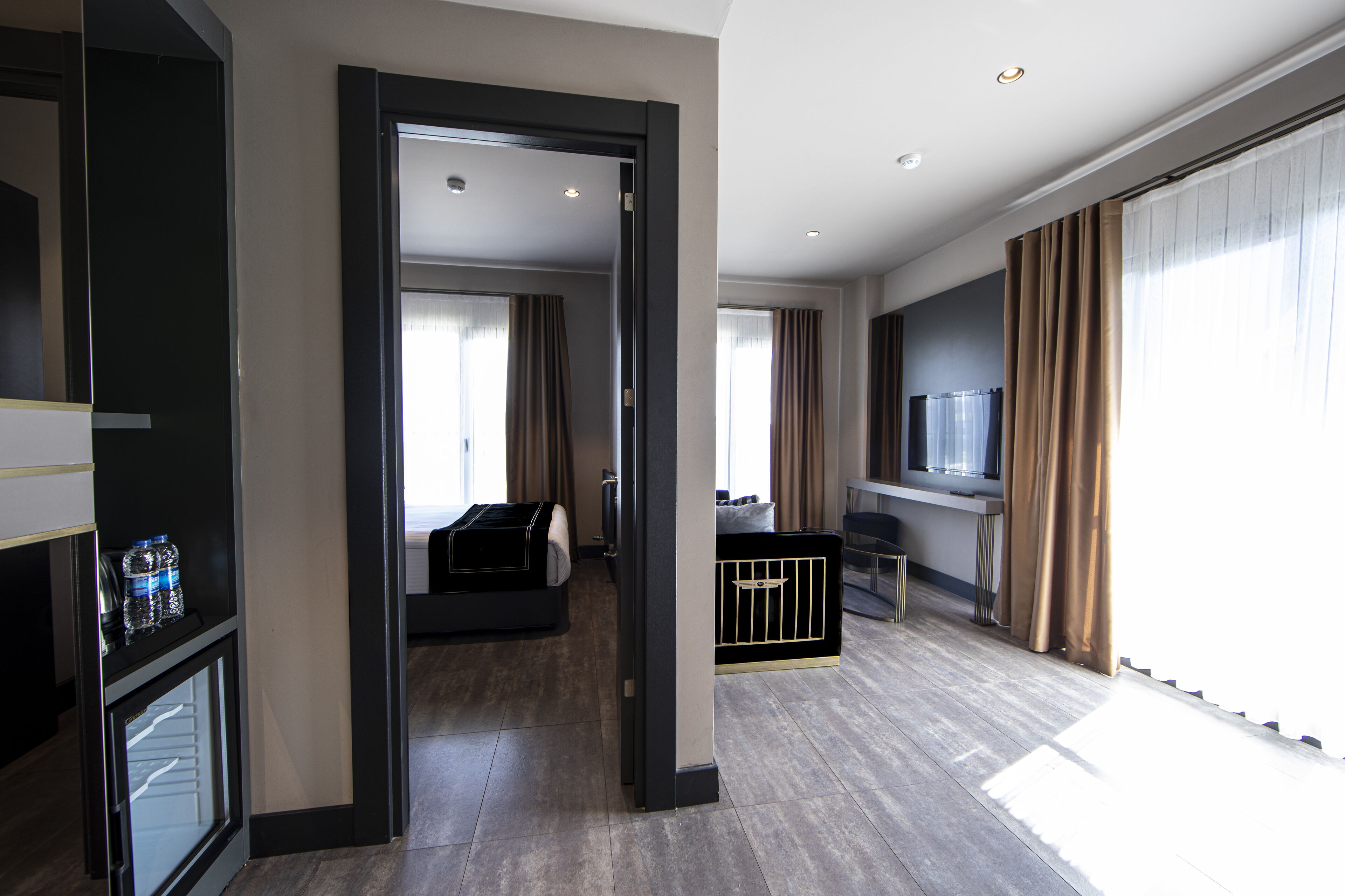 A modern hotel room with a bed, a desk, a TV, and a view of the city.