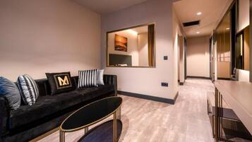 A modern hotel room with a black sofa, a small coffee table, a large mirror, and a TV.