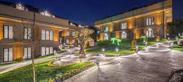 A modern hotel with a well-lit driveway and landscaped garden.