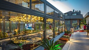 A modern building with large windows, outdoor seating, and a well-lit interior. - Menalo Hotel Premium Istanbul Airport (Arnavutköy)