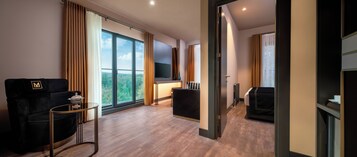 Una habitación de hotel moderna con un ventanal grande, un sofá, un televisor y una mesita.