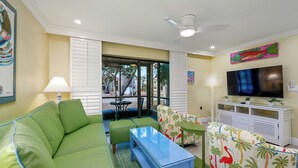 Un salon avec un canapé vert, une table basse bleue et un téléviseur posé sur un meuble blanc.
