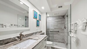 Een moderne badkamer met een marmeren wastafel, een grote spiegel, een glazen douchecabine en een toilet.