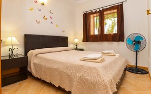 Une chambre à coucher avec un lit, deux lampes de chevet, un ventilateur fixé au mur, une fenêtre avec des rideaux et des autocollants décoratifs représentant des papillons.