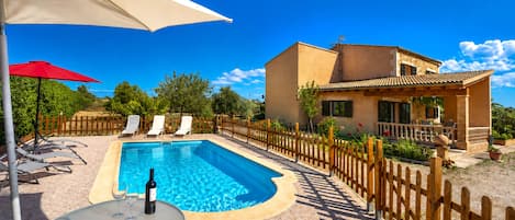 A swimming pool with lounge chairs, a wooden fence, and a building with a tiled roof.