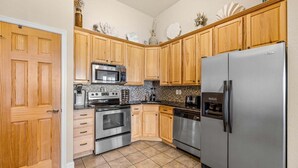 A kitchen with wooden cabinets, a stainless steel refrigerator, a microwave, an oven, and a dishwasher. - FFR309 - Beach Bliss by FIrst Flight Rentals (Kill Devil Hills)