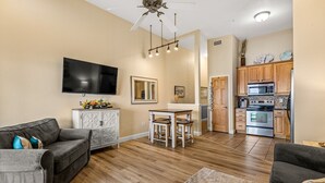 A modern living room with a flat-screen TV, a dining area with a white table and chairs, and a kitchen with wooden cabinets and stainless steel appliances. - FFR309 - Beach Bliss by FIrst Flight Rentals (Kill Devil Hills)
