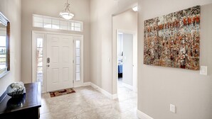 Un couloir avec une porte blanche, un luminaire suspendu, un tapis à motifs et une grande peinture abstraite accrochée au mur.