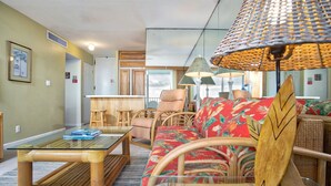Una sala de estar con una mesa de centro de vidrio, muebles de mimbre, un sofá rojo con estampado floral y una lámpara trenzada.