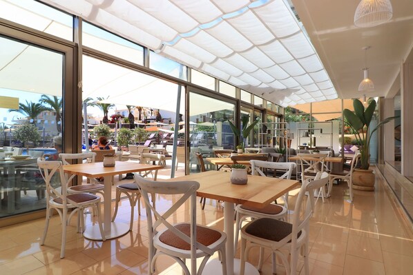 A spacious indoor area with multiple tables and chairs, large windows, and a ceiling with a translucent canopy.