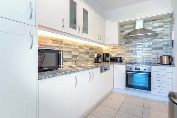 A modern kitchen with white cabinetry, a built-in microwave, a coffee maker, and an oven.