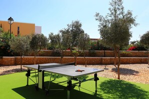 An outdoor ping pong table set up on artificial turf with a stone wall and trees in the background.