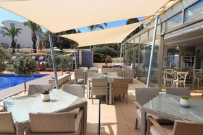 Un patio al aire libre con mesas y sillas, una piscina y un edificio con grandes ventanales.