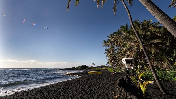 A beach with dark volcanic sand, a rescue boat, and palm trees.