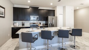 A modern kitchen with dark cabinets, stainless steel appliances, a central island with bar stools, and a white countertop.