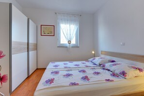 A bedroom with a bed, a window with curtains, a bedside lamp, and a framed picture on the wall.